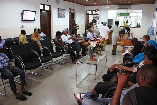 The figure shows a busy emergency waiting room with people sitting on chairs.  The triage desk is in the background.